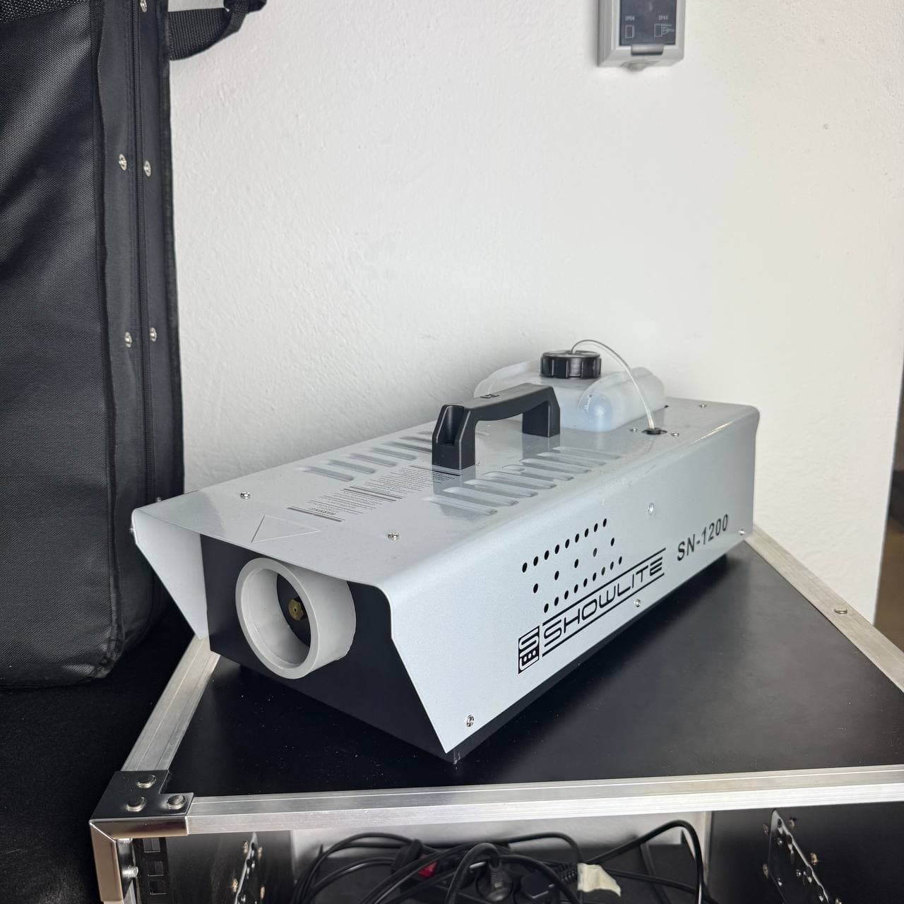 Auf einem schwarzen Gehäuse vor einer weißen Wand steht eine silberne Nebelmaschine mit der Aufschrift „SHOWLITE SN-1200“.