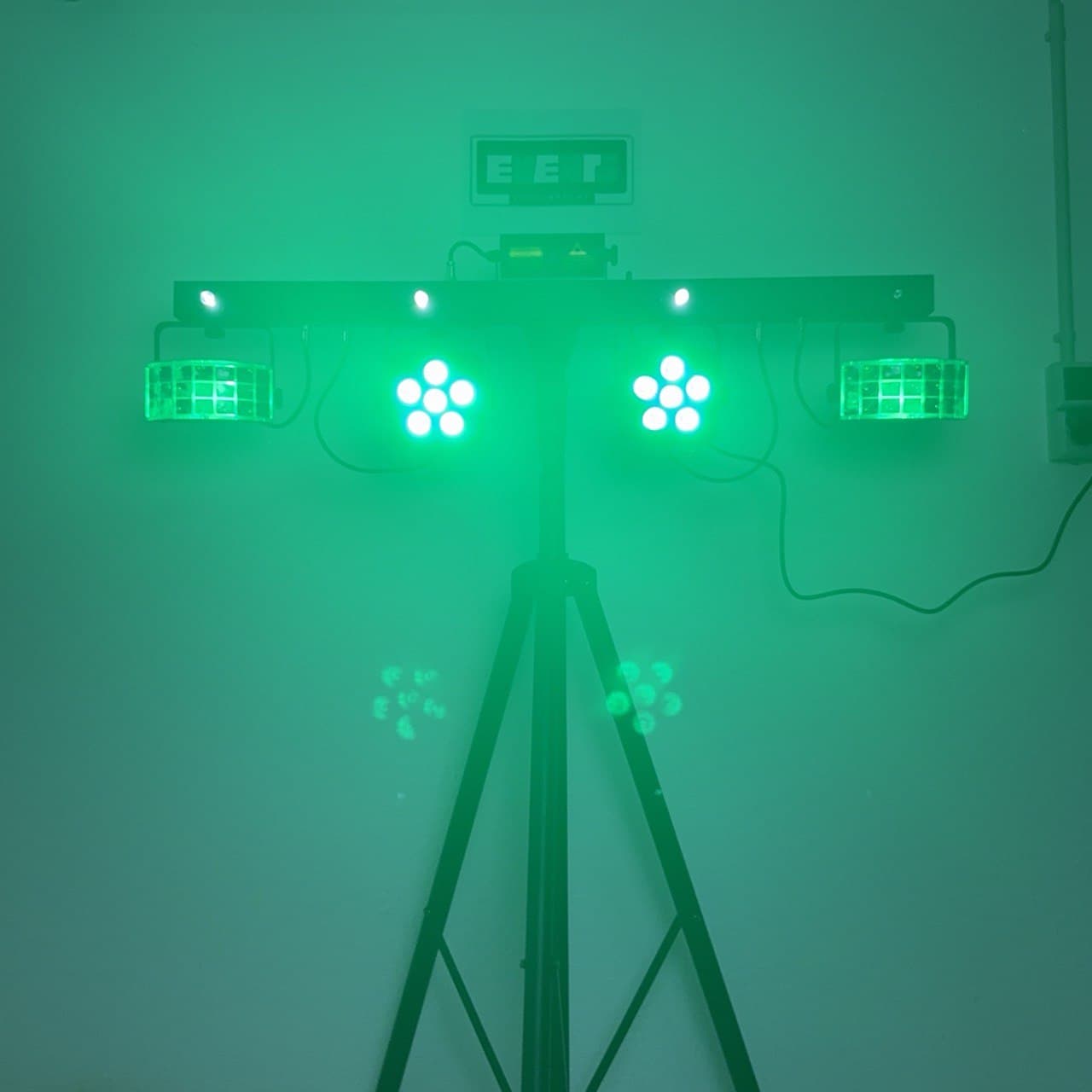 Ein grün beleuchtetes, auf einem Stativ montiertes Bühnenlichtset mit mehreren quadratischen Lampen, die einen hellen Schein vor einem schlichten Hintergrund werfen.