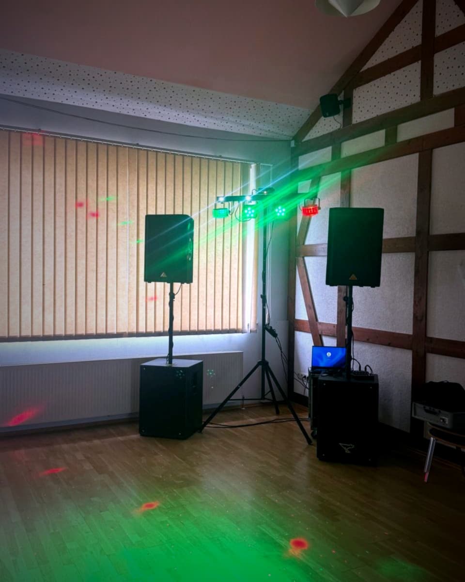 Lautsprecher und Beleuchtungsgeräte sind in einem Raum mit Holzböden und getäfelten Wänden aufgestellt und strahlen bunte Lichter für eine Veranstaltung aus.