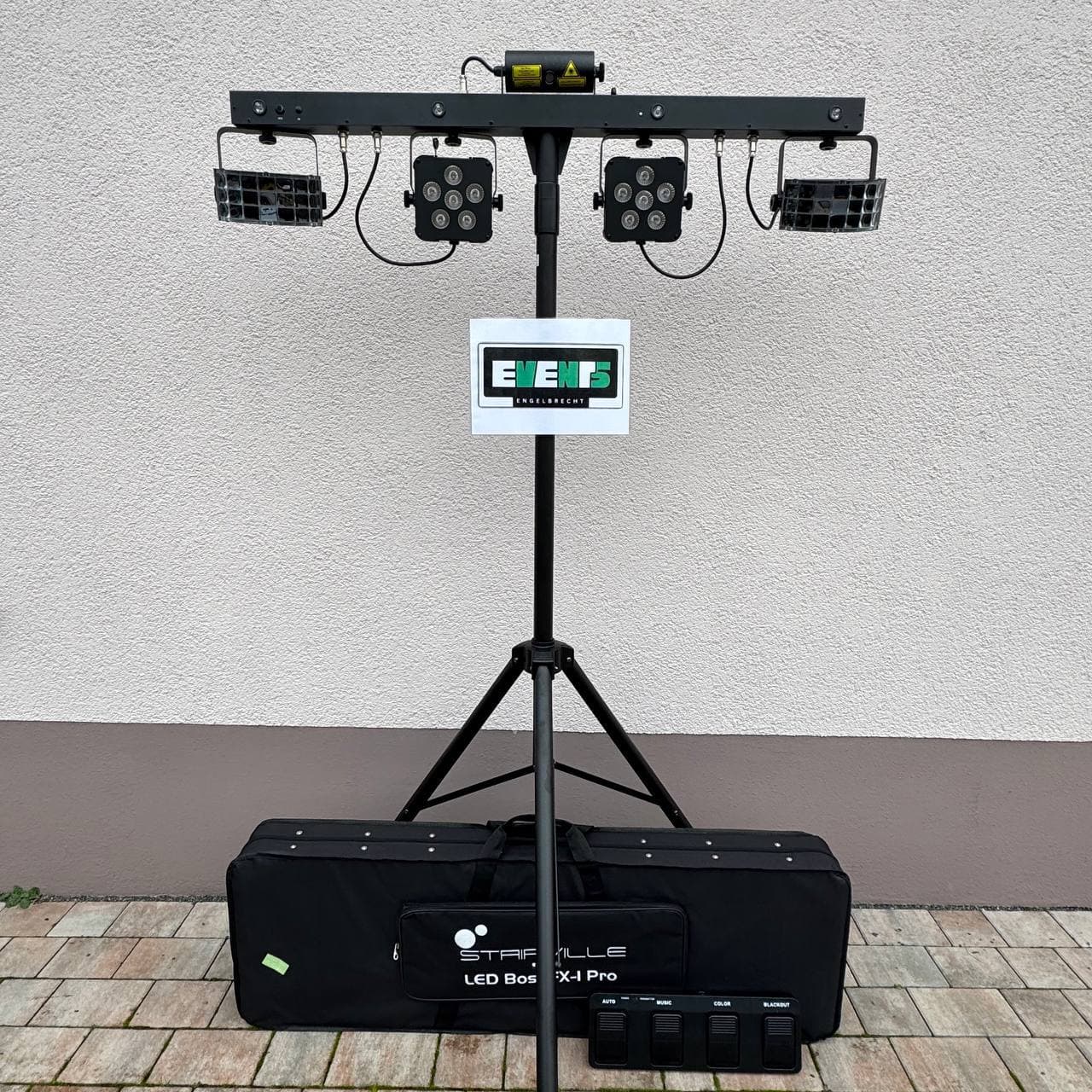 Aufbau einer LED-Bühnenbeleuchtung auf einem Stativ mit mehreren verstellbaren Leuchten, einer Tragetasche und einem Bedienfeld auf einer gepflasterten Fläche